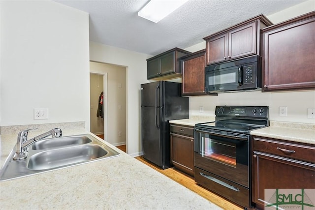 kitchen featuring light wood finished floors, black appliances, light countertops, a textured ceiling, and a sink