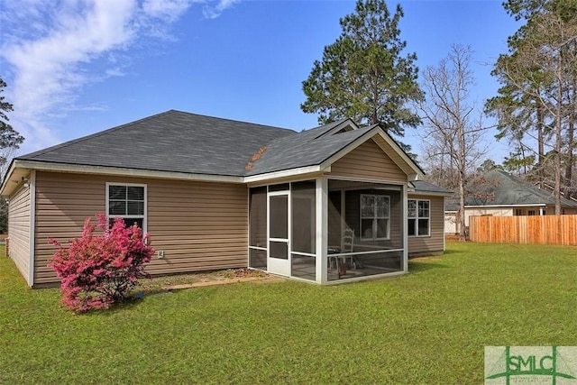 back of property with a sunroom, a lawn, a shingled roof, and fence