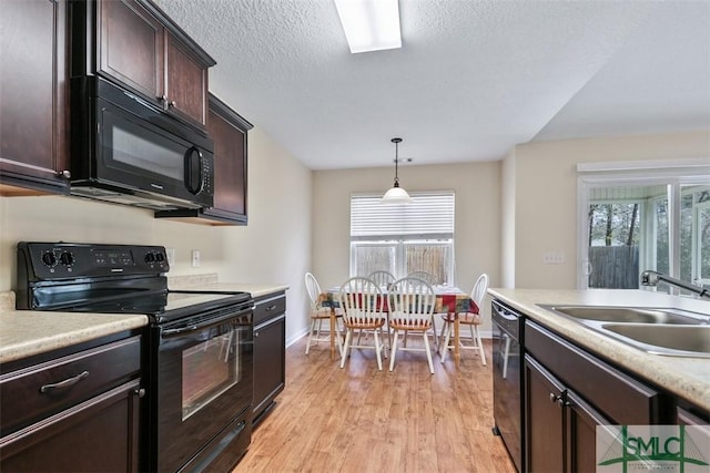 kitchen with black appliances, light wood-style flooring, a sink, decorative light fixtures, and light countertops