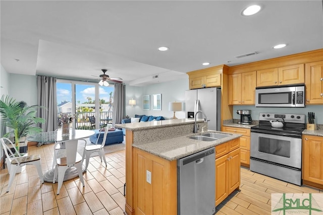 kitchen with a center island with sink, a sink, open floor plan, appliances with stainless steel finishes, and wood tiled floor