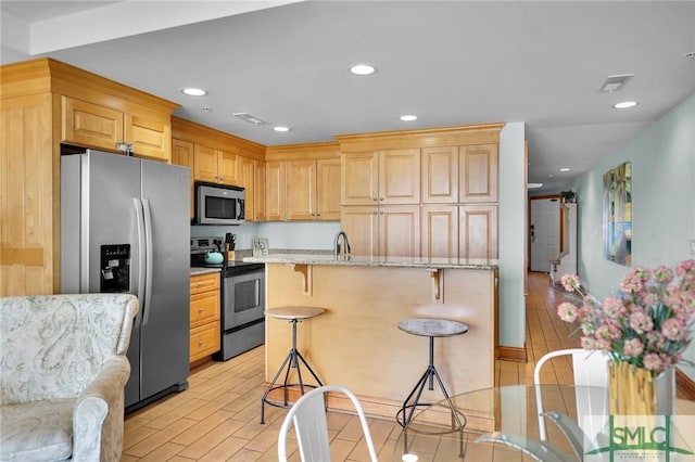 kitchen with visible vents, a breakfast bar, light stone counters, recessed lighting, and appliances with stainless steel finishes