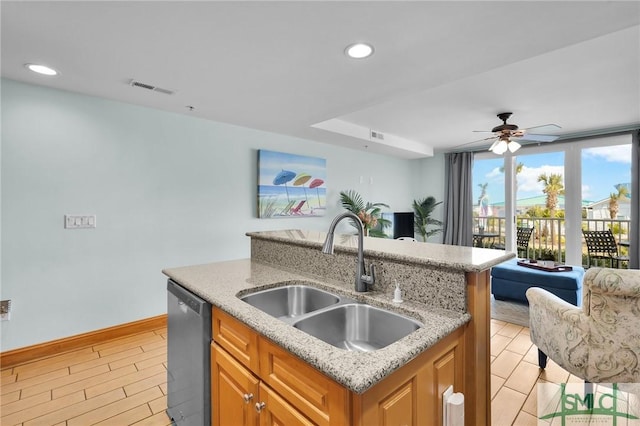 kitchen featuring light stone counters, a kitchen island with sink, a sink, dishwasher, and open floor plan