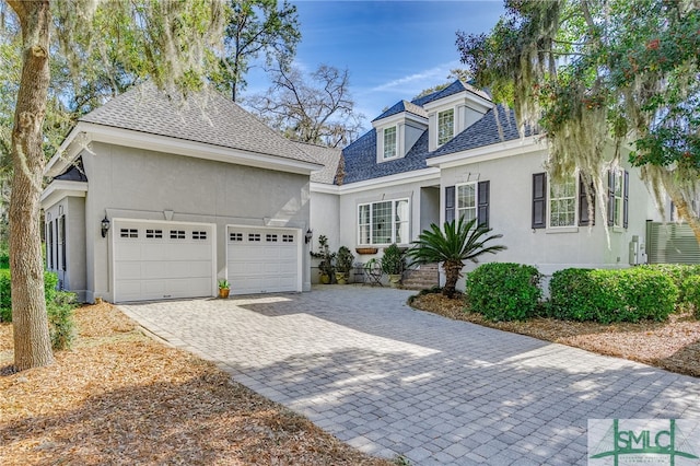 view of front of home featuring stucco siding, an attached garage, decorative driveway, and roof with shingles