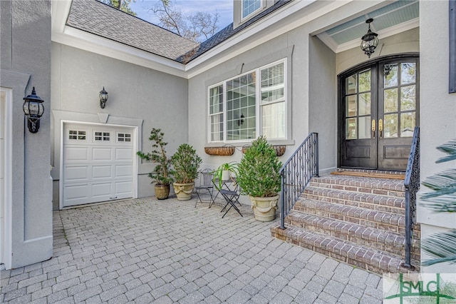 view of exterior entry with a garage, stucco siding, french doors, and roof with shingles