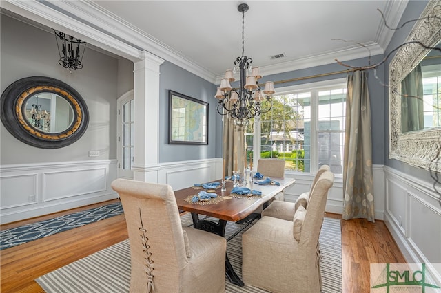 dining space featuring visible vents, a chandelier, a wainscoted wall, ornamental molding, and wood finished floors