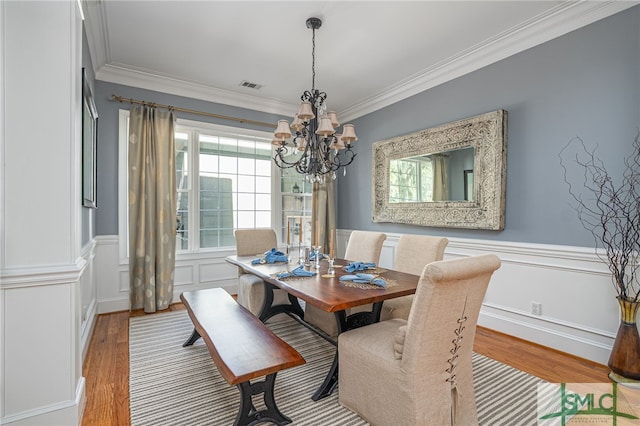 dining space with wood finished floors, wainscoting, and ornamental molding