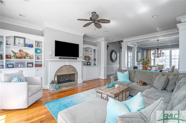 living area featuring built in shelves, a fireplace with flush hearth, wood finished floors, crown molding, and ornate columns