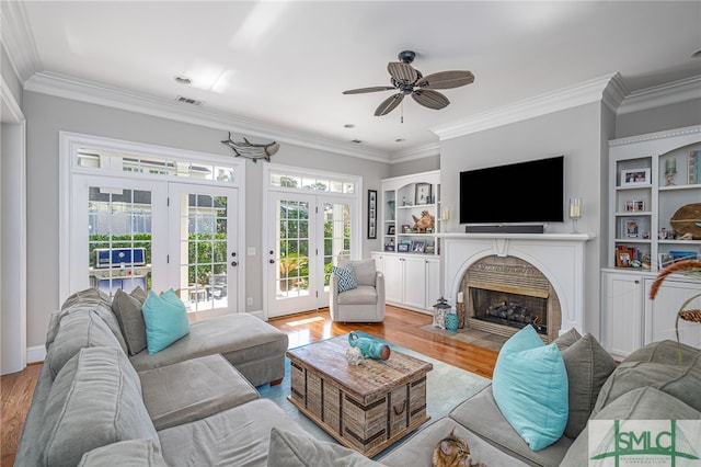 living area featuring visible vents, built in shelves, crown molding, a fireplace with flush hearth, and wood finished floors