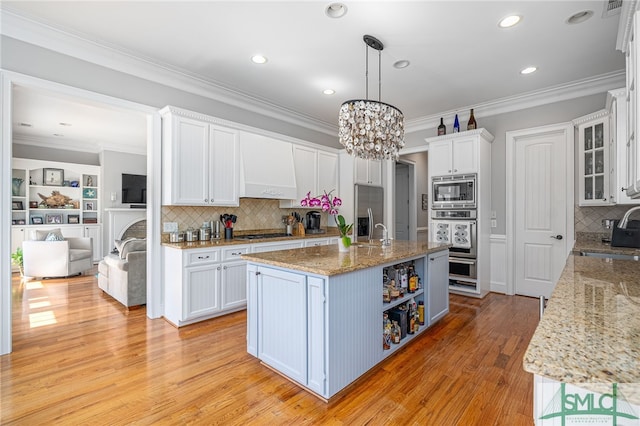 kitchen with custom exhaust hood, light wood-style flooring, ornamental molding, appliances with stainless steel finishes, and white cabinetry