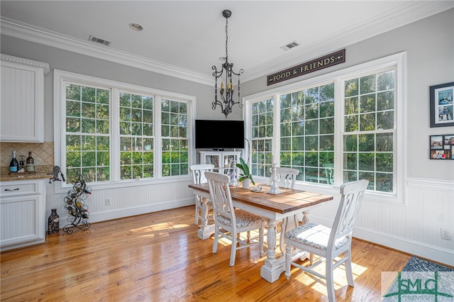 dining room with ornamental molding, light wood-style floors, visible vents, and wainscoting