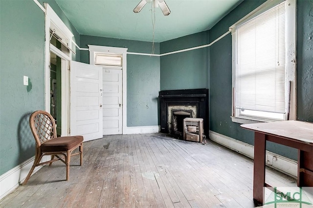 living room with baseboard heating, baseboards, wood-type flooring, and ceiling fan