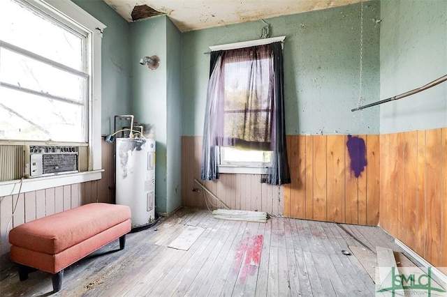 unfurnished room with wooden walls, wainscoting, wood-type flooring, and electric water heater