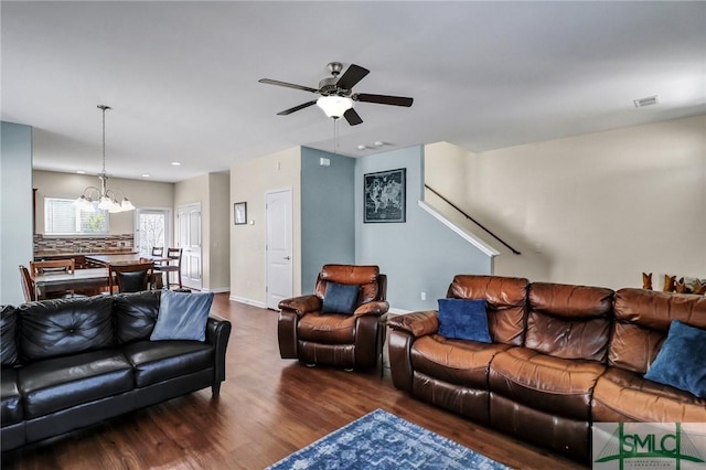 living area with ceiling fan with notable chandelier, dark wood-style floors, visible vents, and baseboards