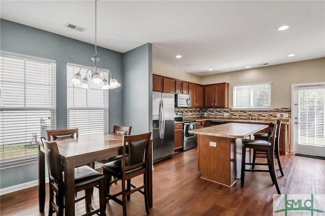 kitchen with dark wood-style floors, visible vents, a kitchen island, decorative backsplash, and appliances with stainless steel finishes