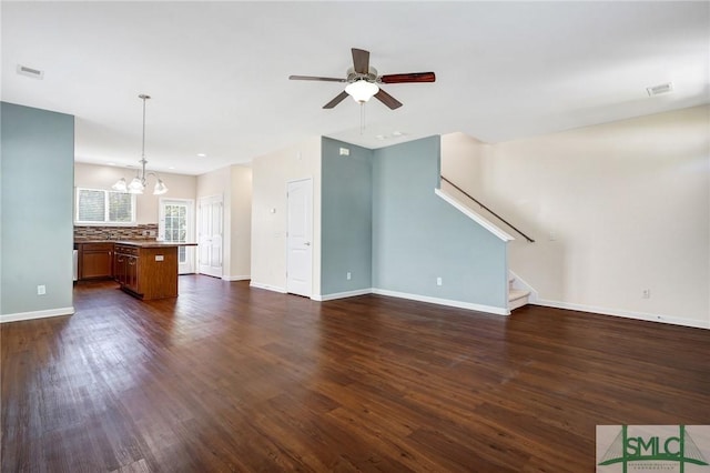 unfurnished living room with visible vents, baseboards, stairway, dark wood finished floors, and ceiling fan with notable chandelier