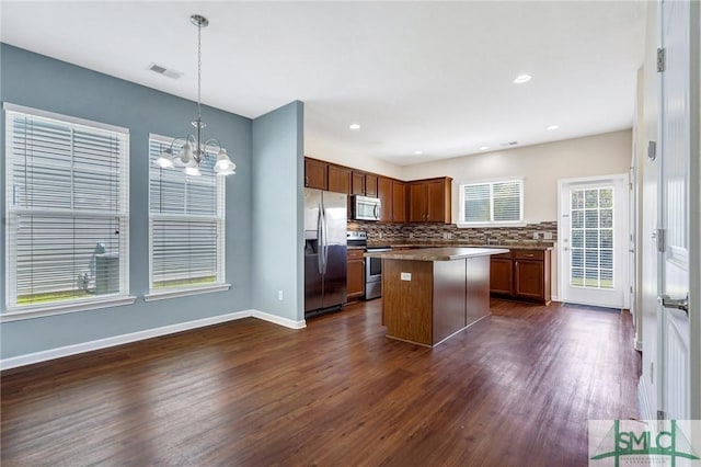 kitchen with a kitchen island, backsplash, dark wood finished floors, an inviting chandelier, and stainless steel appliances