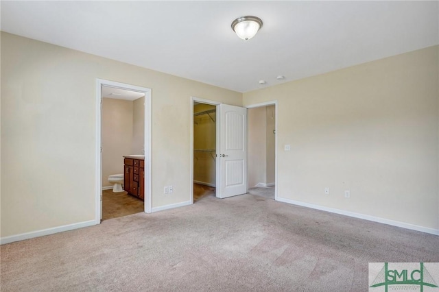 unfurnished bedroom with connected bathroom, carpet, baseboards, a spacious closet, and a closet