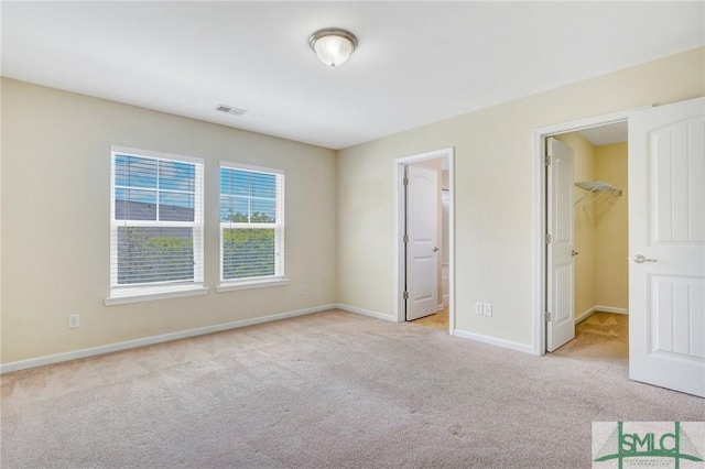 unfurnished bedroom featuring visible vents, light colored carpet, baseboards, a closet, and a spacious closet