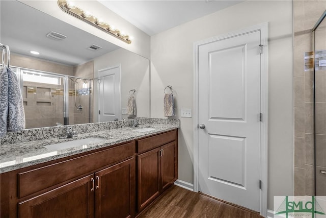 full bathroom with a sink, double vanity, wood finished floors, and a shower stall