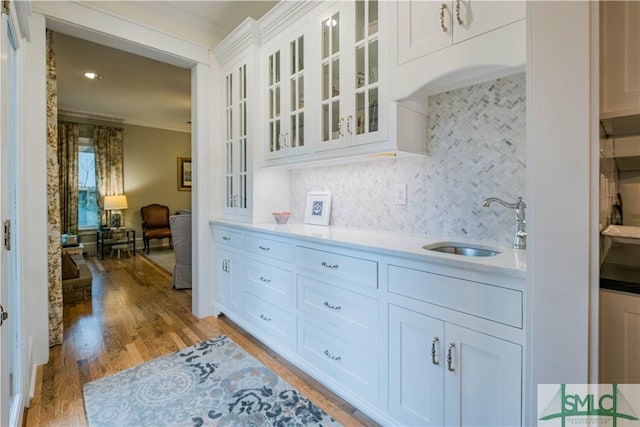 kitchen with light wood-style flooring, a sink, decorative backsplash, light countertops, and glass insert cabinets