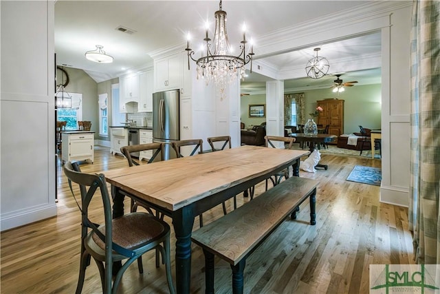 dining space featuring visible vents, crown molding, light wood-type flooring, lofted ceiling, and ceiling fan with notable chandelier