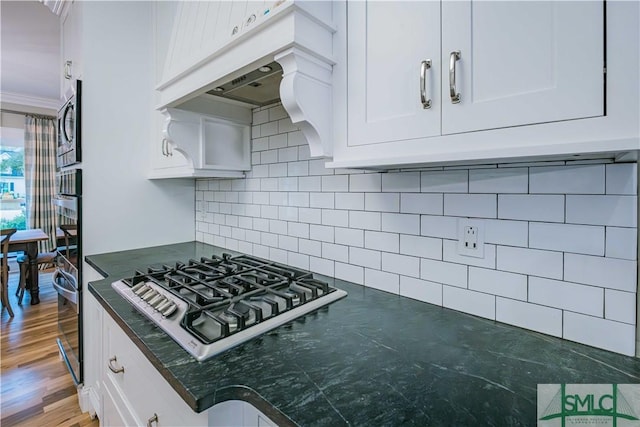 kitchen with tasteful backsplash, crown molding, extractor fan, stainless steel appliances, and white cabinetry