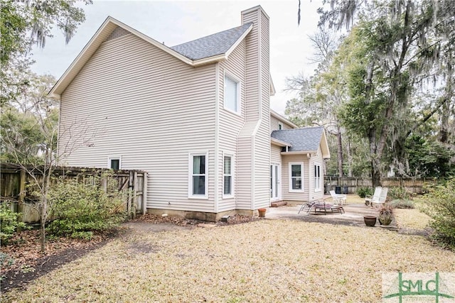 rear view of house featuring a patio area, a shingled roof, a chimney, and fence