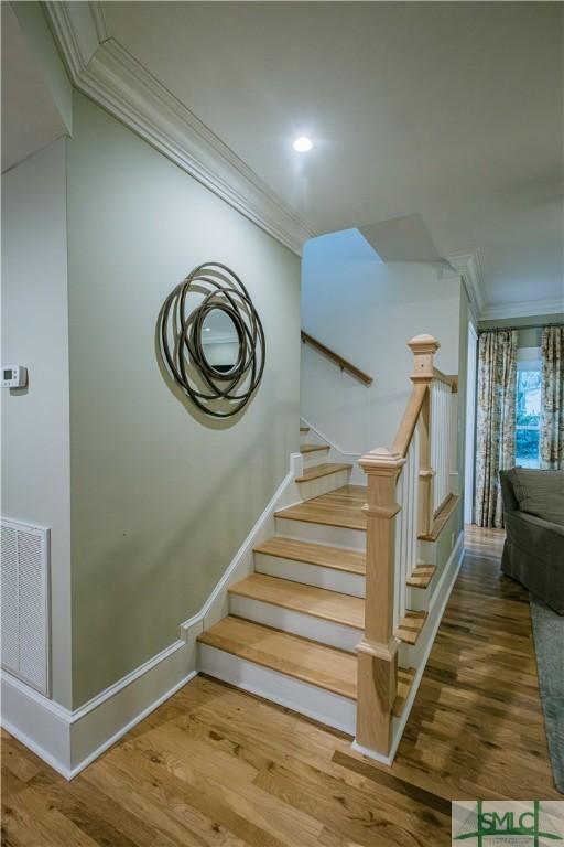 stairway with baseboards, wood finished floors, visible vents, and ornamental molding