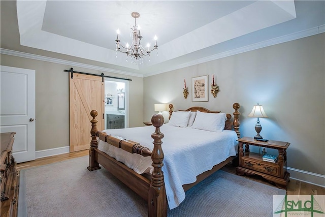 bedroom featuring a barn door, a tray ceiling, and wood finished floors