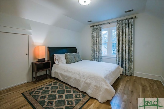 bedroom with vaulted ceiling, visible vents, baseboards, and wood finished floors