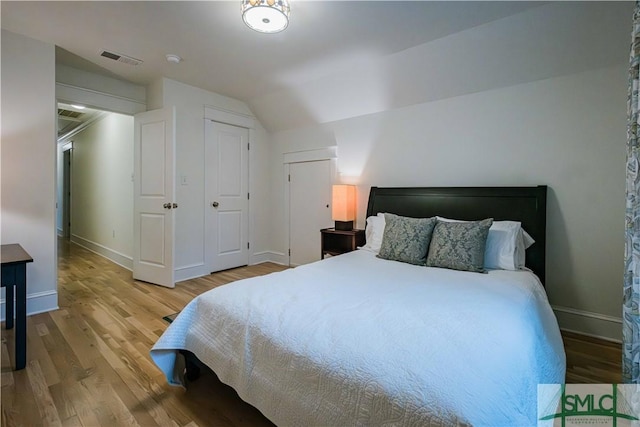 bedroom featuring vaulted ceiling, visible vents, baseboards, and wood finished floors