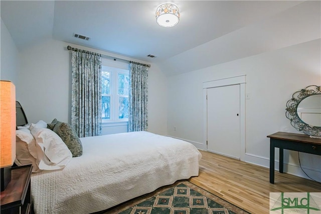 bedroom featuring visible vents, baseboards, wood finished floors, and vaulted ceiling