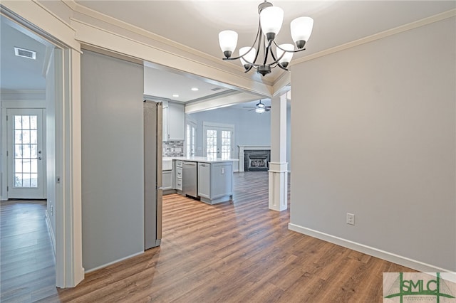 unfurnished dining area with visible vents, ornamental molding, ceiling fan with notable chandelier, a fireplace, and wood finished floors