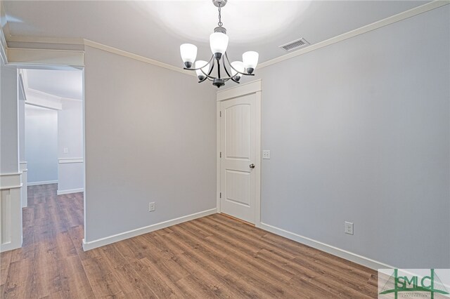 empty room featuring visible vents, wood finished floors, an inviting chandelier, and ornamental molding