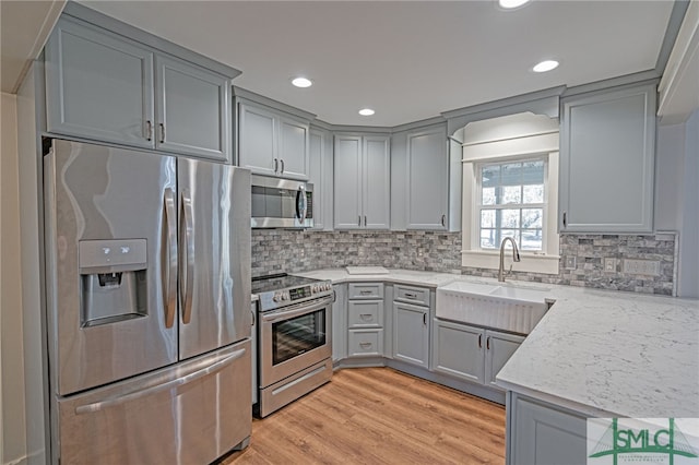 kitchen featuring a sink, stainless steel appliances, light wood-style floors, and gray cabinetry