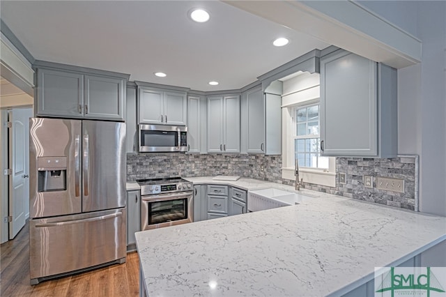 kitchen with gray cabinetry, a sink, wood finished floors, stainless steel appliances, and a peninsula