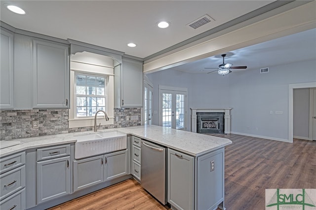 kitchen with tasteful backsplash, gray cabinets, a peninsula, a fireplace, and stainless steel dishwasher