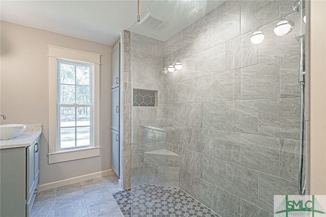 full bathroom with a tile shower, visible vents, vanity, and a wealth of natural light