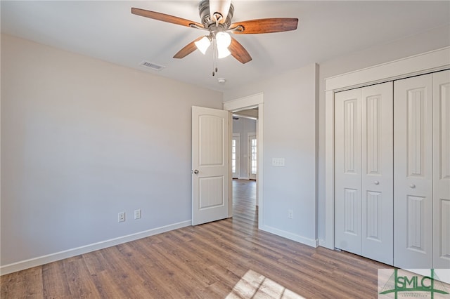 unfurnished bedroom featuring wood finished floors, visible vents, a closet, and baseboards