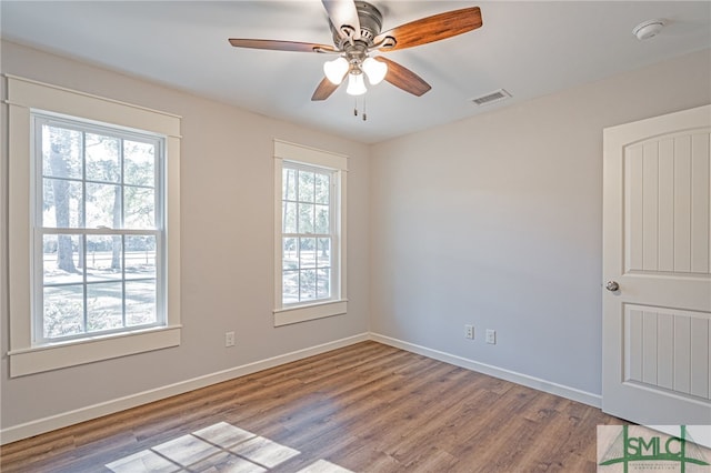 unfurnished room with a ceiling fan, wood finished floors, visible vents, and baseboards