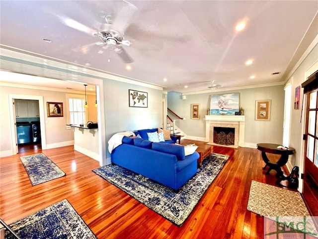 living room featuring a tiled fireplace, hardwood / wood-style floors, a ceiling fan, and ornamental molding