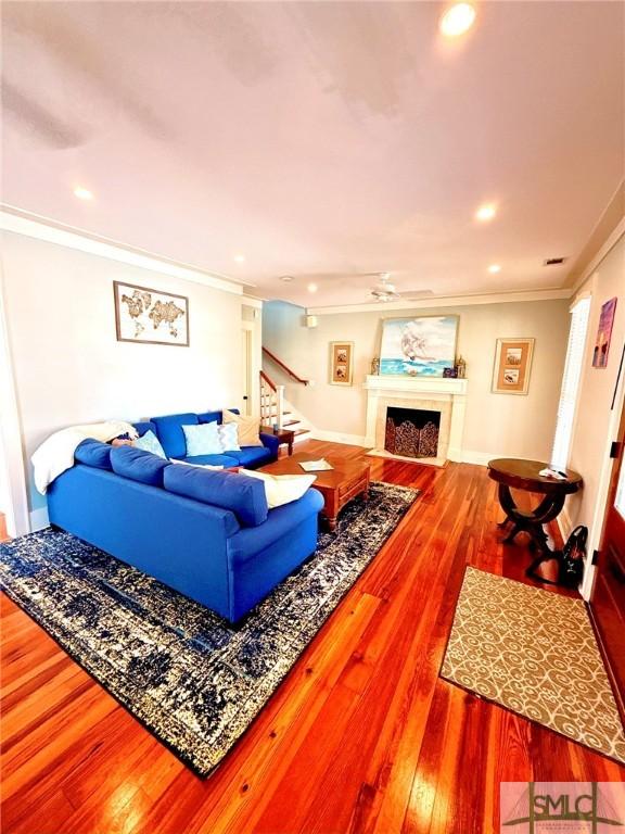 living room featuring stairway, a fireplace with flush hearth, wood finished floors, and ornamental molding