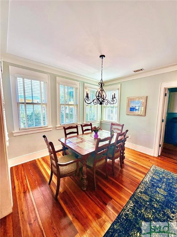 dining space with visible vents, a notable chandelier, crown molding, light wood finished floors, and baseboards