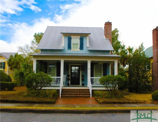 view of front of house with a porch, a chimney, and metal roof