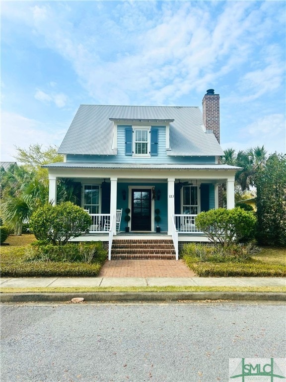 farmhouse-style home featuring metal roof, a chimney, and covered porch
