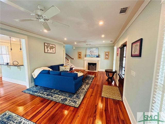 living area featuring hardwood / wood-style flooring, stairway, a ceiling fan, visible vents, and ornamental molding