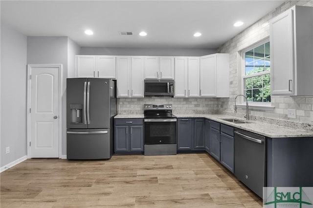 kitchen featuring a sink, appliances with stainless steel finishes, white cabinets, light wood finished floors, and light stone countertops