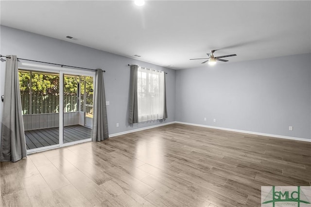 spare room with a ceiling fan, visible vents, wood finished floors, and baseboards