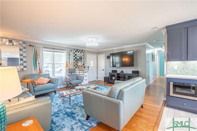 living area featuring visible vents, baseboards, light wood-style floors, and ornamental molding