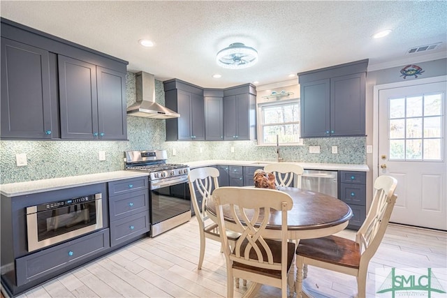 kitchen with light wood-style flooring, a sink, stainless steel appliances, light countertops, and wall chimney exhaust hood